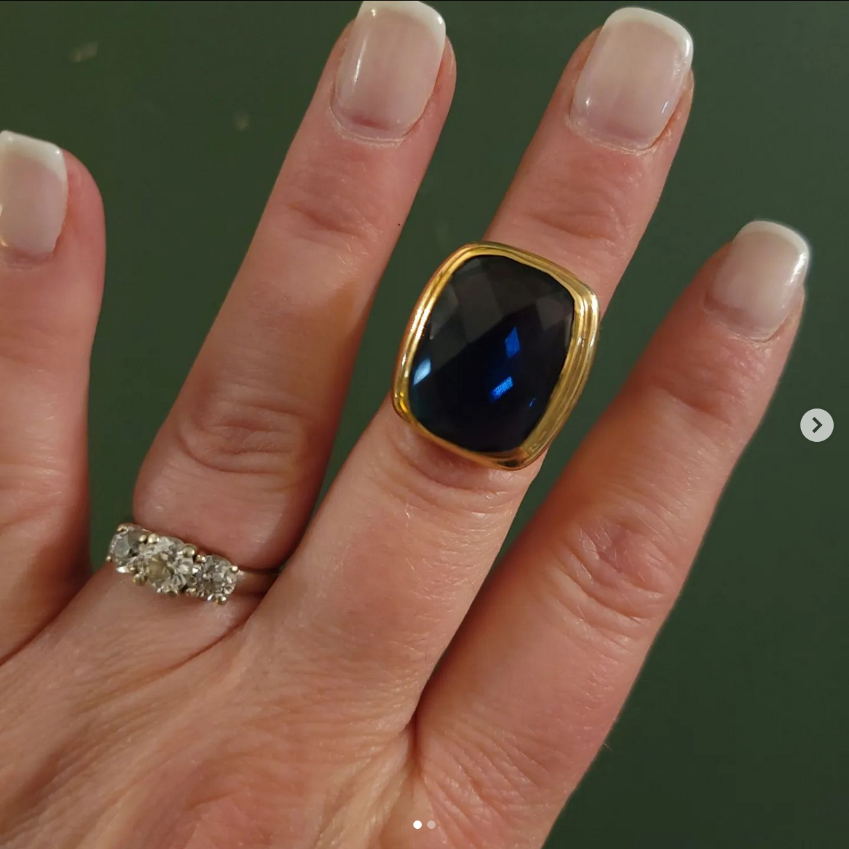 Blue and gold ring and diamond ring on a hand in front of a green background