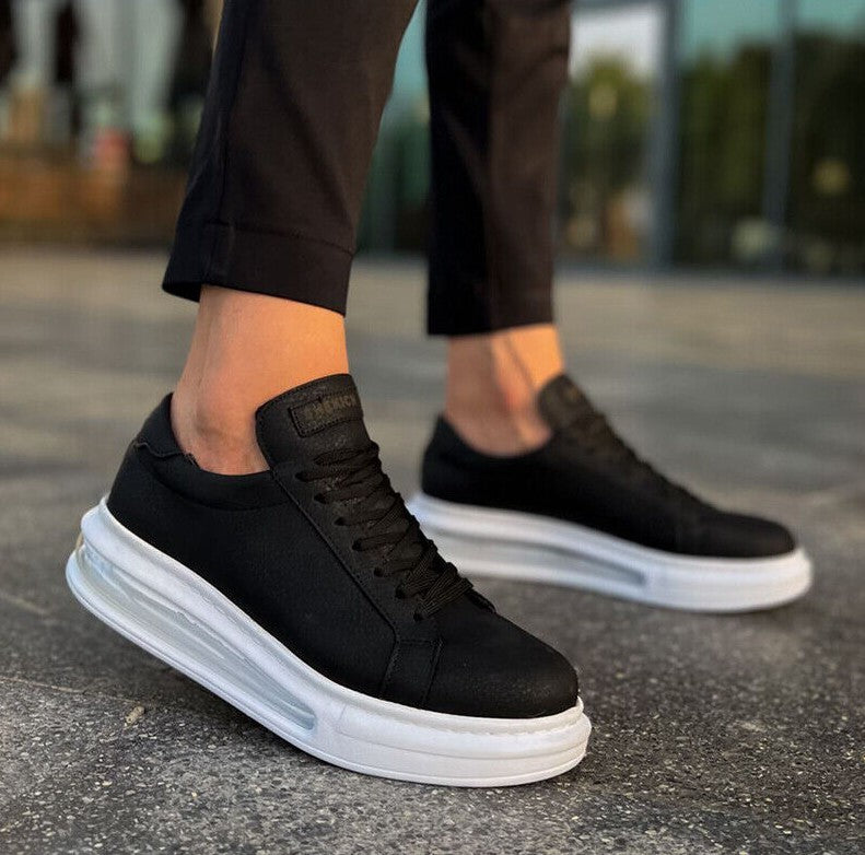 Black sneakers with white soles worn by a person on a blurred outdoor background